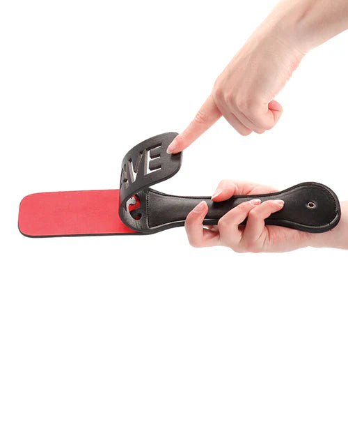 A hand demonstrating the paddle's unique design, showcasing its dual-sided functionality with the word 'SLAVE' artfully cut out.