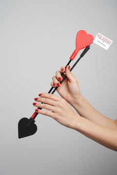 Fetish Fantasy silicone heart crop flogger with red and black design, held by woman's hands against a light grey background.