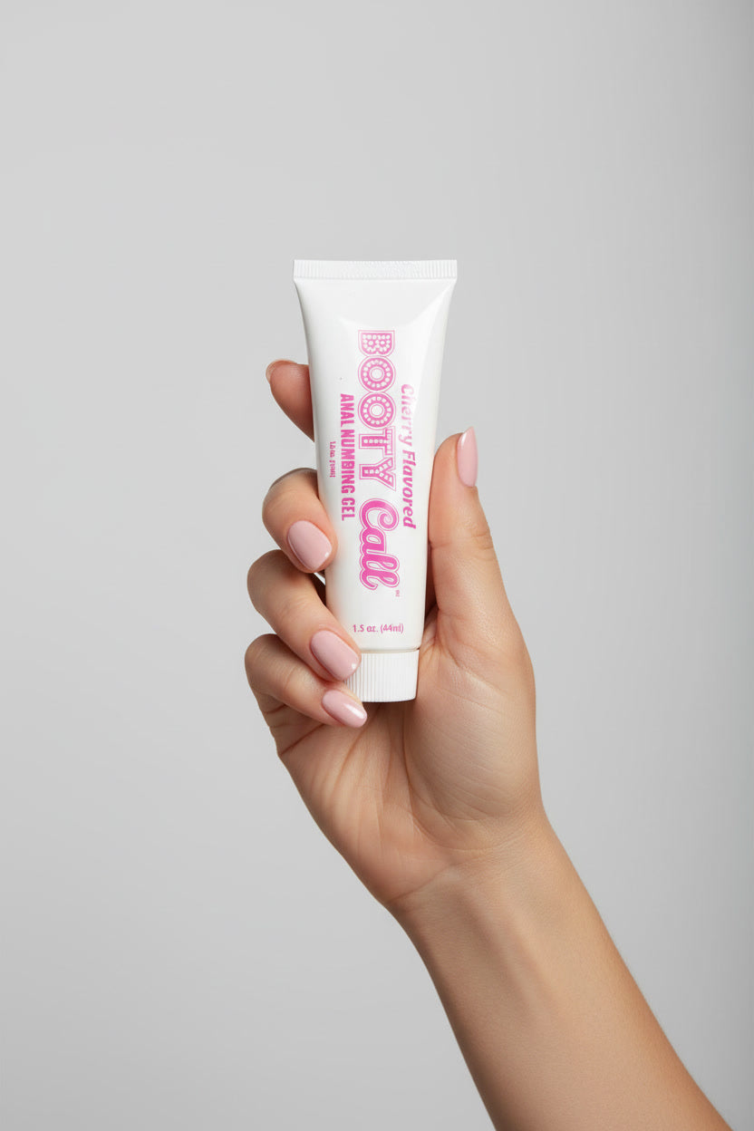 Little Genie Booty Call Anal Numbing Gel in cherry flavor, 1.5oz, shown with a woman’s hand holding the tube against a light grey background.