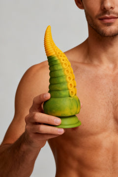 Creature Cocks Monstropus 2.0 vibrating silicone dildo held by a shirtless man, showcasing its light grey color and tentacle design.