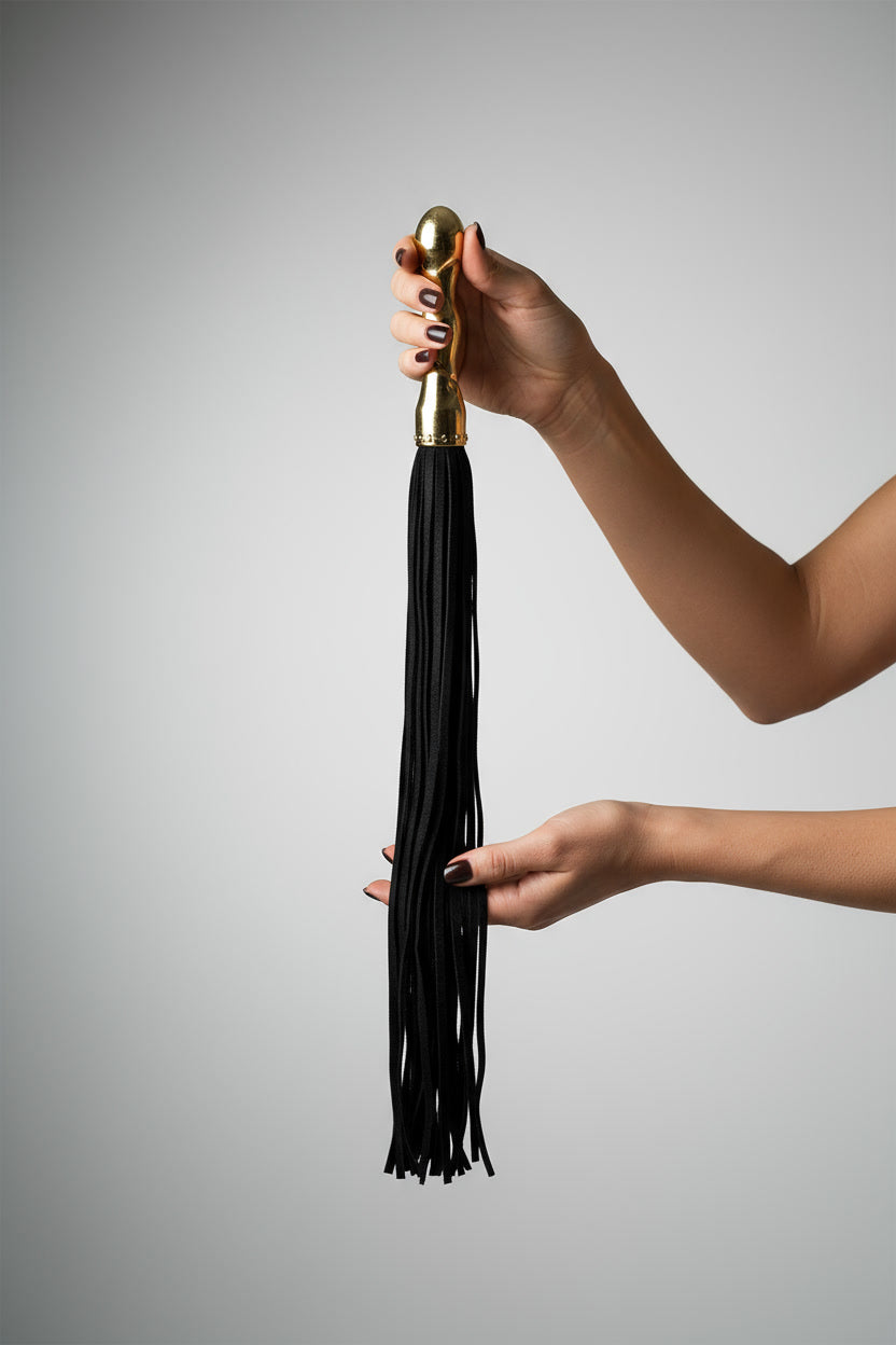 Hands holding the Ouch! Luxury Whip by Shots, a sleek flogger with a leather handle and multiple leather tails, on a light grey background.