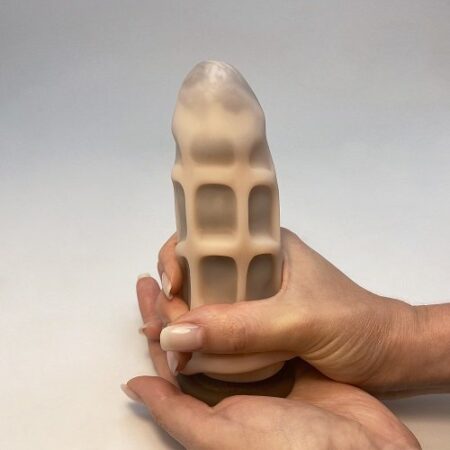 a woman's manicured hand stretching a masturbator toy over a dildo
