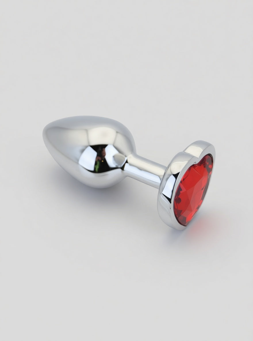 Toosh heart-shaped metal butt plug with red stone, available in small, medium, and large sizes, shiny metallic finish.
