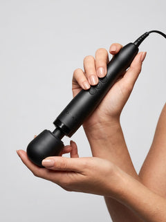 Doxy 2.0 Original Plug-In Massage Wand Vibrator held in both hands, showing the black massage wand controls and soft rounded head